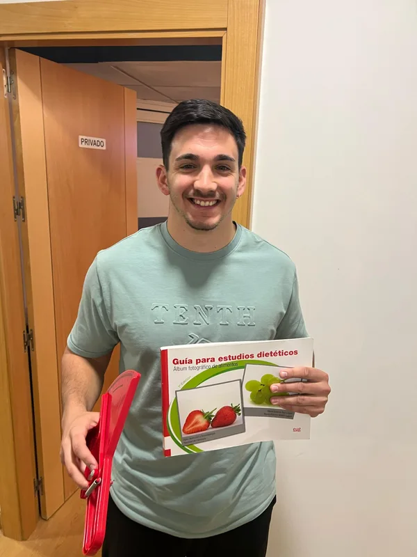 Christian Rodríguez Granados, dietista-nutricionista, de pie con una guía de alimentación y un plicómetro